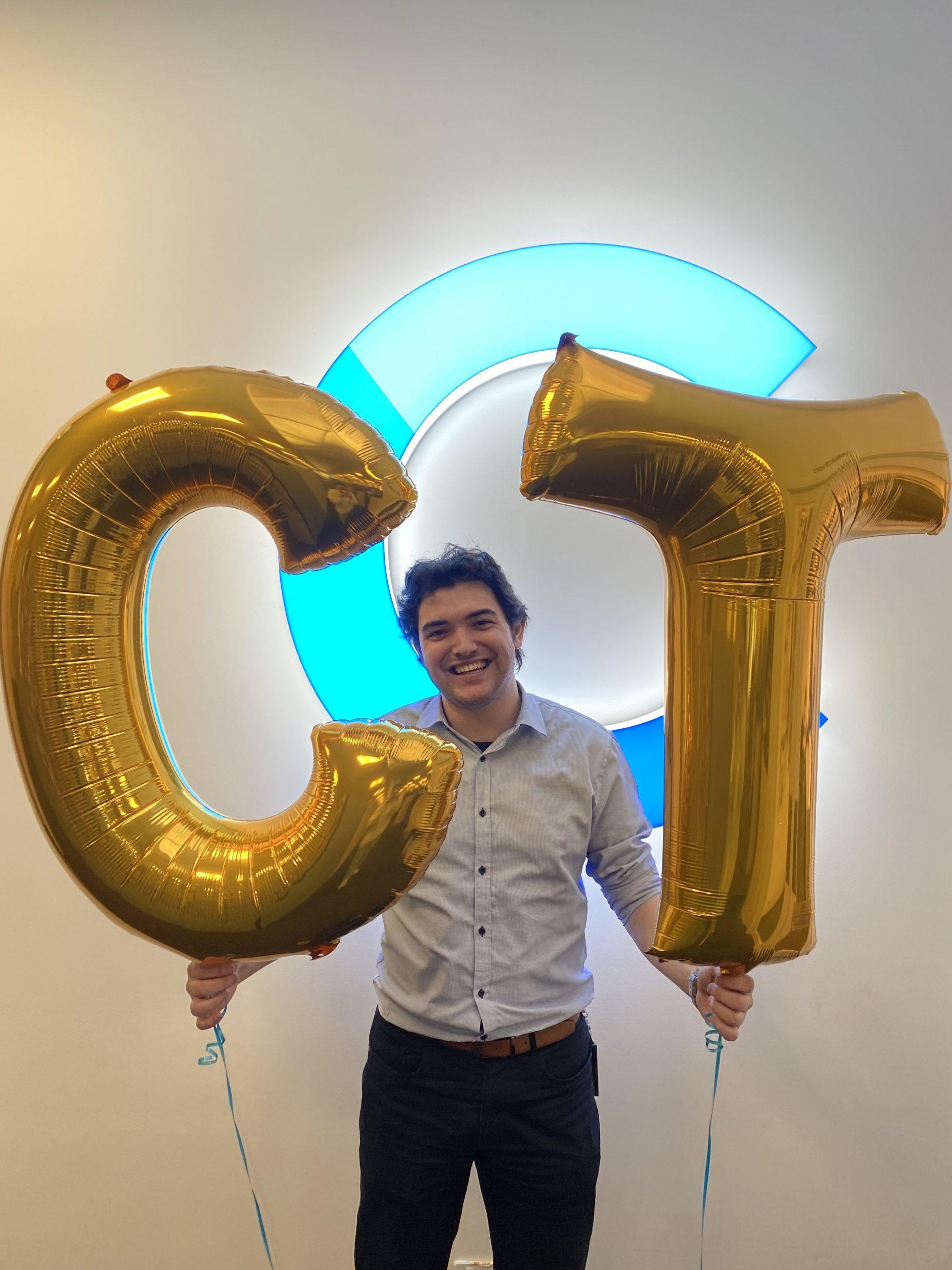 A CT employee holding gold CT baloons, in front of the CT logo